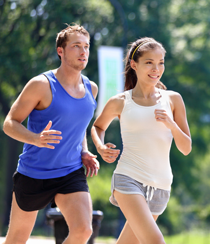 Paar joggt in sportlicher Kleidung, Männer in blauem Shirt, Frauen in weißem Top, Parkhintergrund.