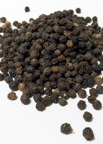 Eine Menge schwarzer Pfefferkörner auf weißem Untergrund, lose verstreut, verschiedene Größen und Farben.