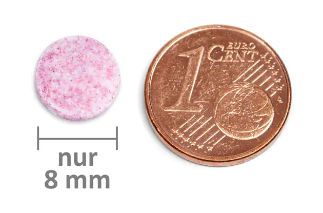 Rosa Brausetablette mit einem Durchmesser von 8 mm neben einer 1-Cent-Münze für Größenvergleich.