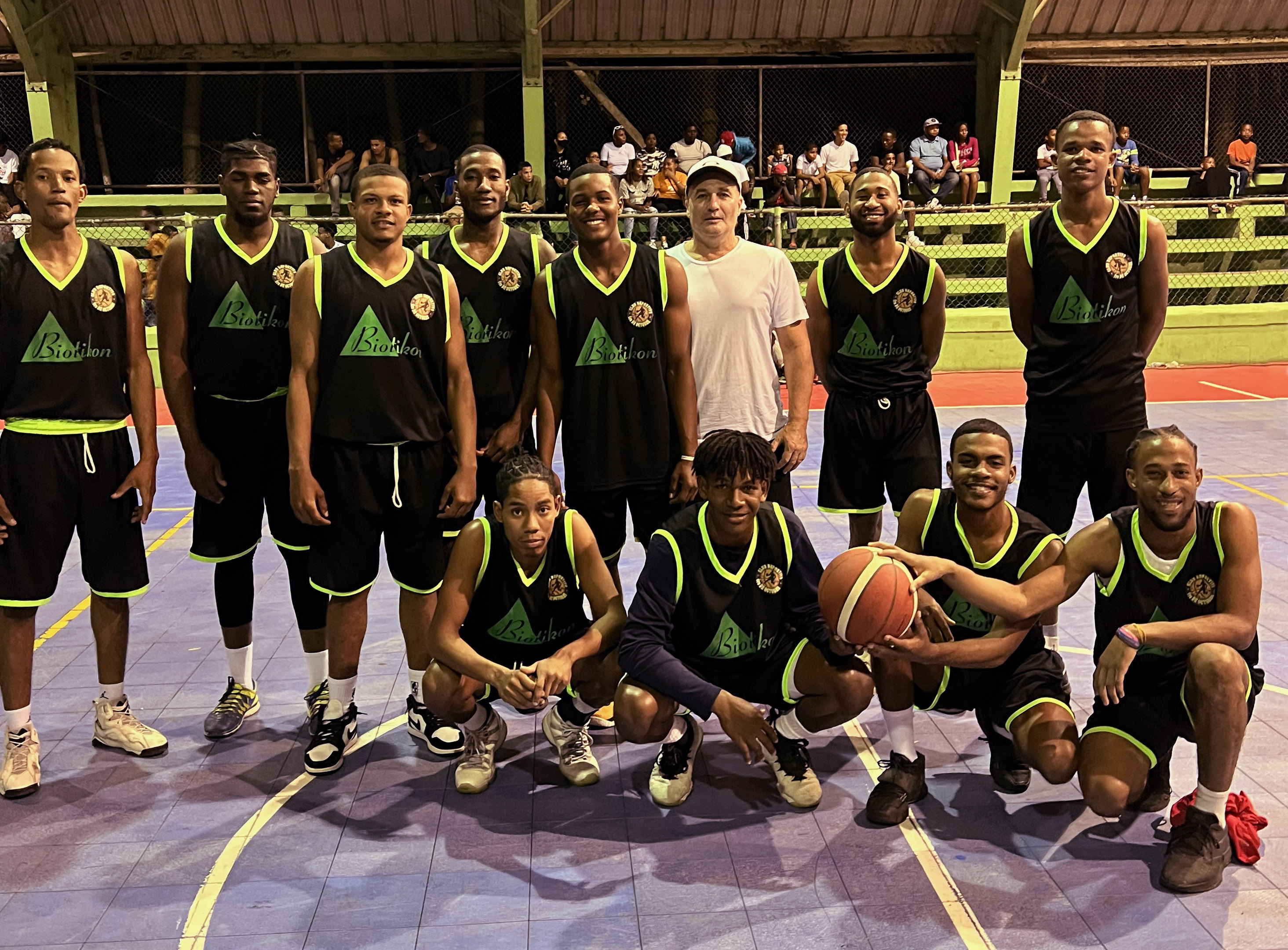 Eine Gruppe von Basketballspielern in schwarzen Trikots mit grünen Akzenten, auf dem Spielfeld stehend, mit Basketball und jubelnder Pose.