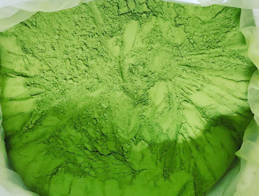 Feines, grünes Pulver in einer Verpackung, gut sichtbar. Pulver hat eine leuchtende grüne Farbe und eine gleichmäßige Textur.