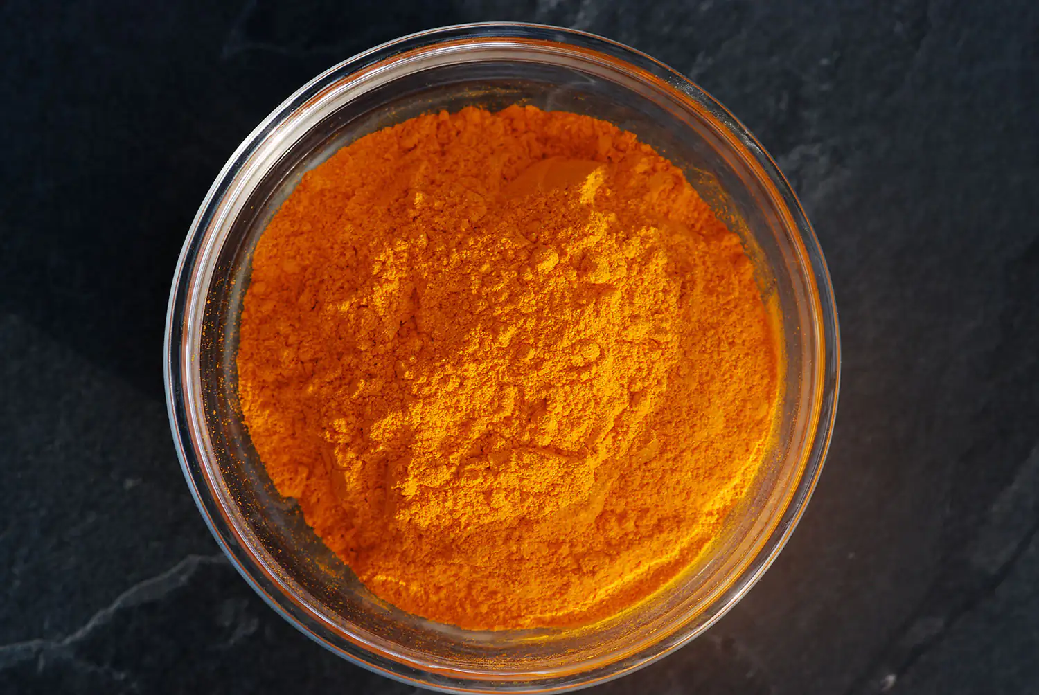 Oranges Kurkuma Pulver in einem Glasbehälter, 100 g, von oben aufgenommen.
